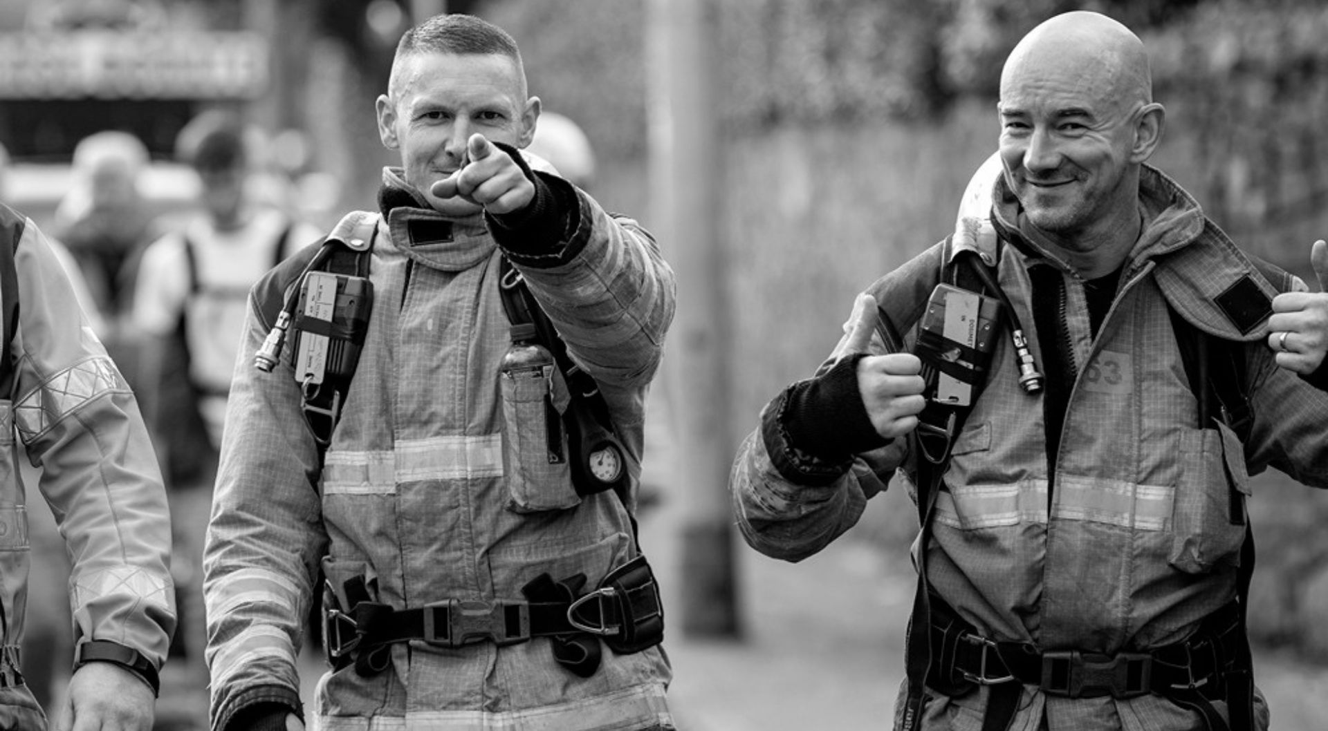 Two fire fighters walking, one pointing at the camera