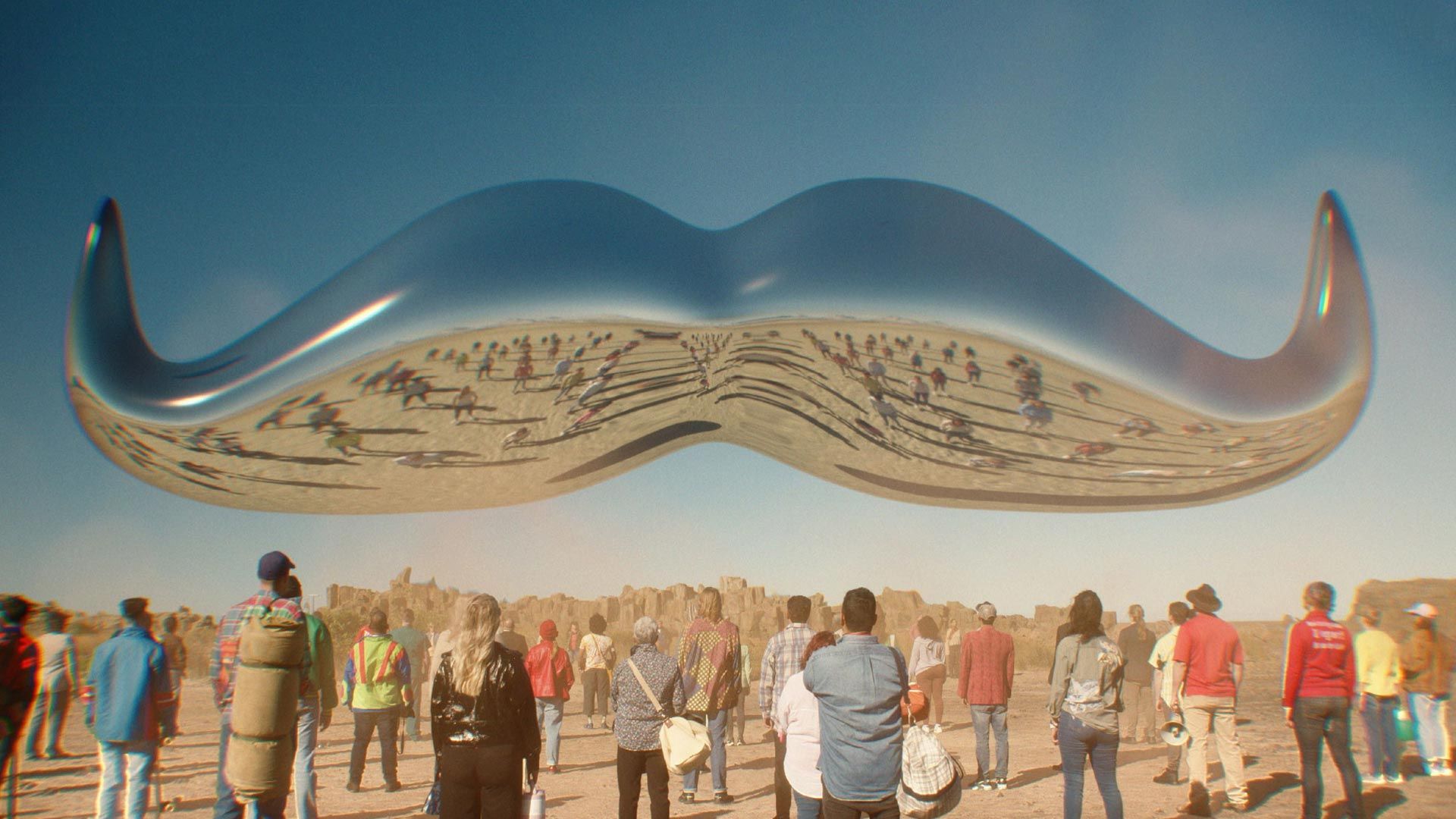 A crowd of people gathered around a floating chrome moustache.