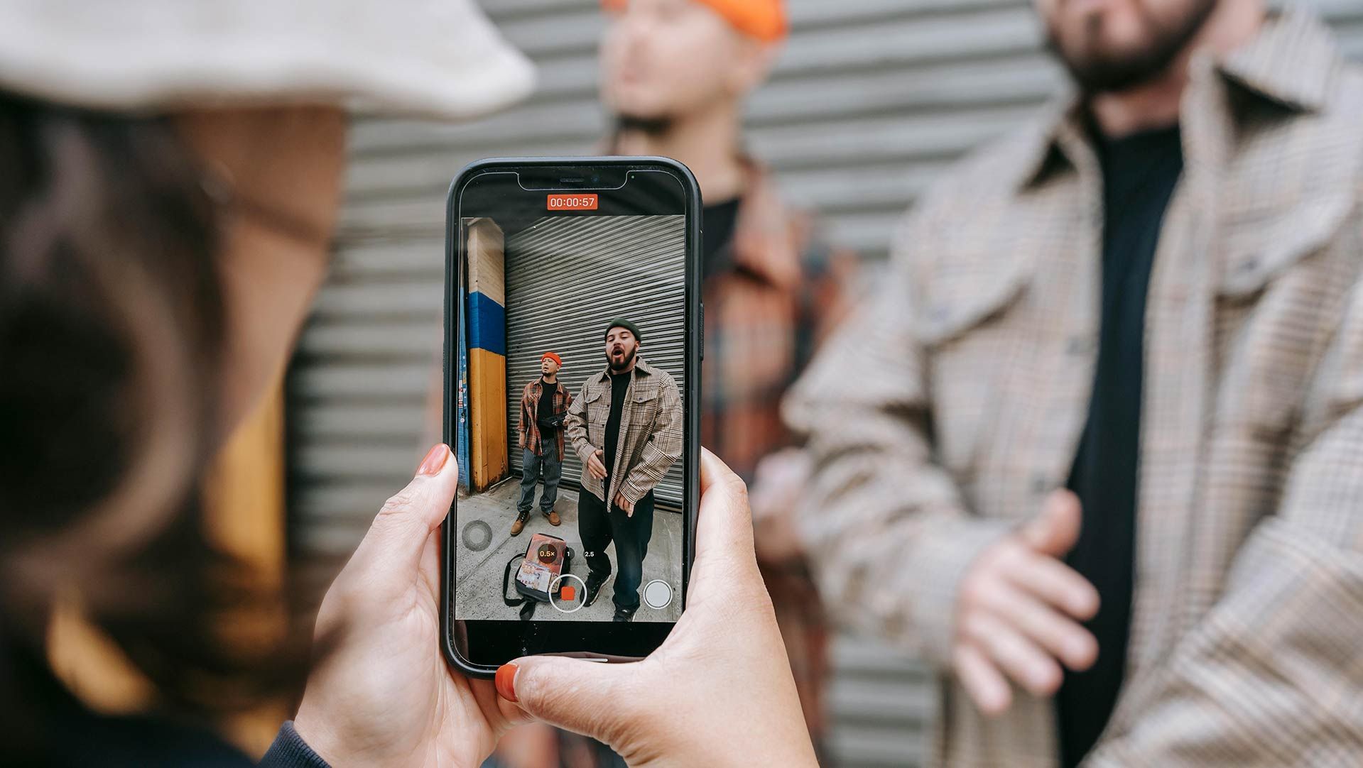 Photo of a man filming another man on his smartphone.